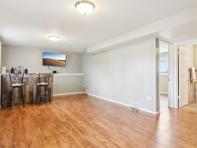 living room featuring light wood-style floors, baseboards, a bar, and visible vents