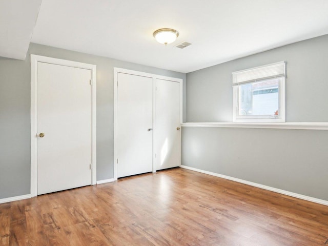 unfurnished bedroom with visible vents, baseboards, two closets, and wood finished floors