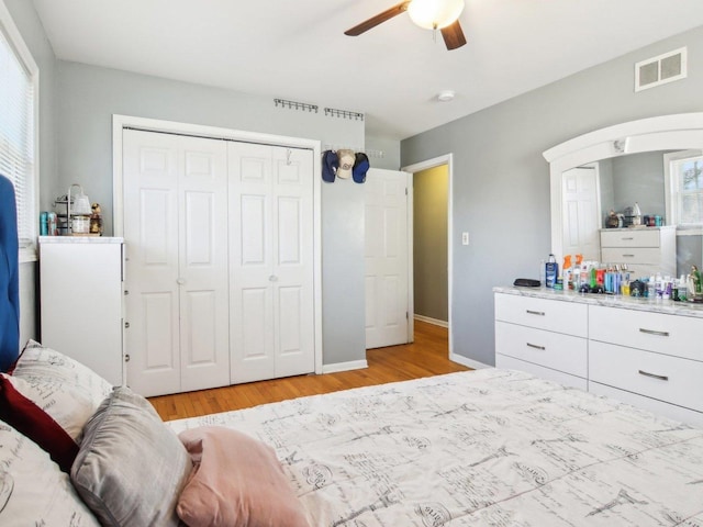 bedroom featuring a ceiling fan, visible vents, light wood finished floors, baseboards, and a closet