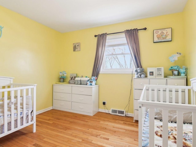 bedroom featuring a crib, visible vents, baseboards, and wood finished floors