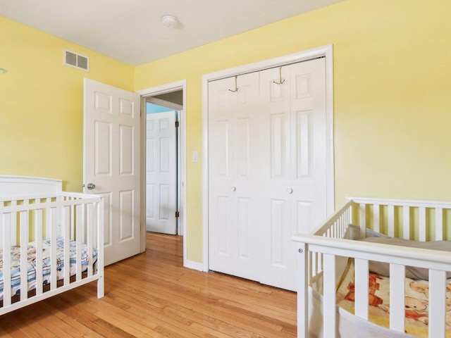 bedroom with a closet, visible vents, light wood-type flooring, and baseboards