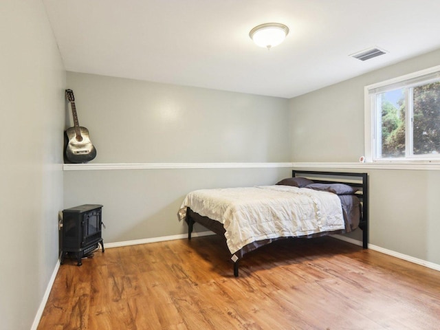 bedroom featuring a wood stove, wood finished floors, visible vents, and baseboards