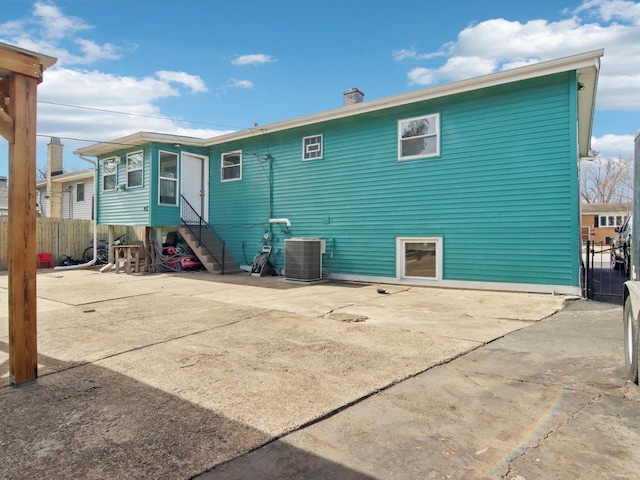 rear view of property featuring entry steps, fence, central AC unit, a chimney, and a patio area