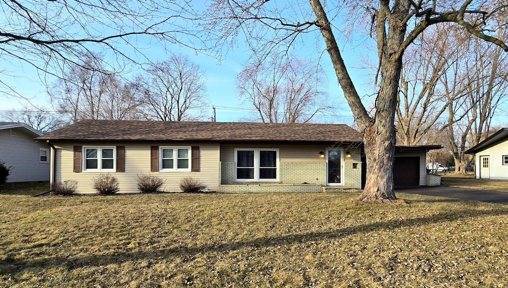 ranch-style home featuring aphalt driveway, an attached garage, brick siding, and a front yard