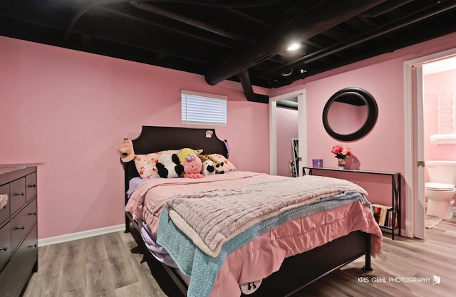 bedroom featuring beam ceiling, light wood-style flooring, connected bathroom, and baseboards