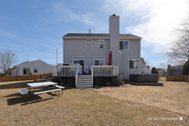 rear view of property with fence, a yard, a wooden deck, a chimney, and a hot tub