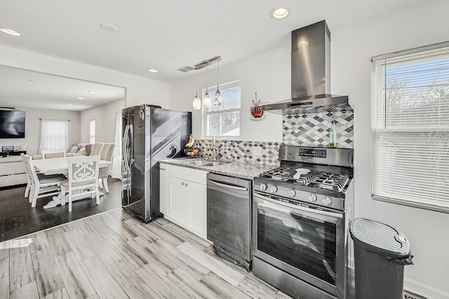 kitchen featuring a sink, backsplash, stainless steel appliances, light wood-style floors, and wall chimney range hood