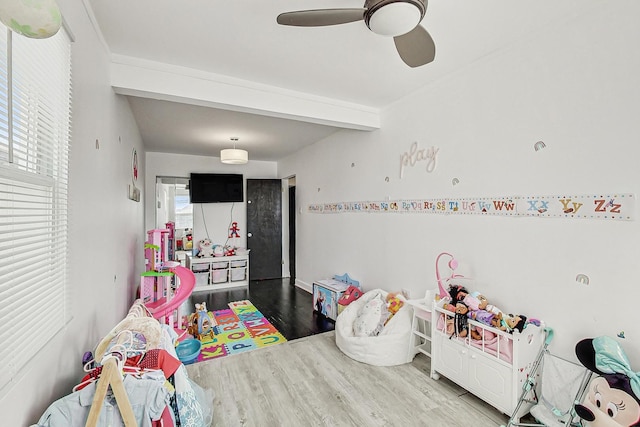 recreation room with ceiling fan, beamed ceiling, and wood finished floors