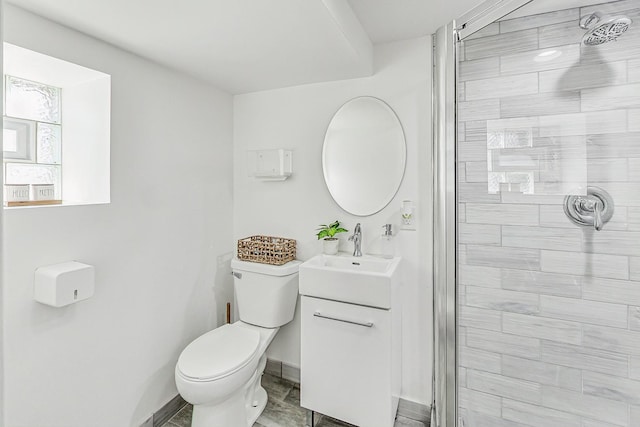 full bathroom featuring a tile shower, toilet, vanity, and baseboards