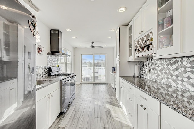 kitchen with white cabinetry, dark stone counters, wall chimney range hood, and stainless steel gas range