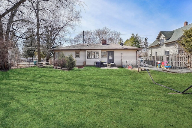 rear view of house with a chimney, a yard, and fence