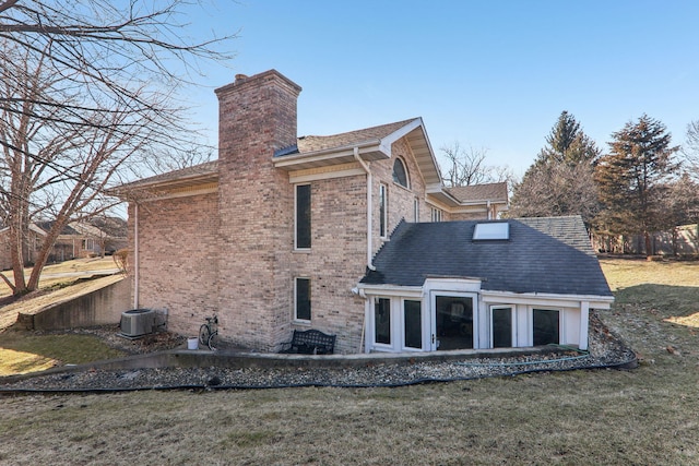 back of property featuring brick siding, central AC, roof with shingles, a lawn, and a chimney