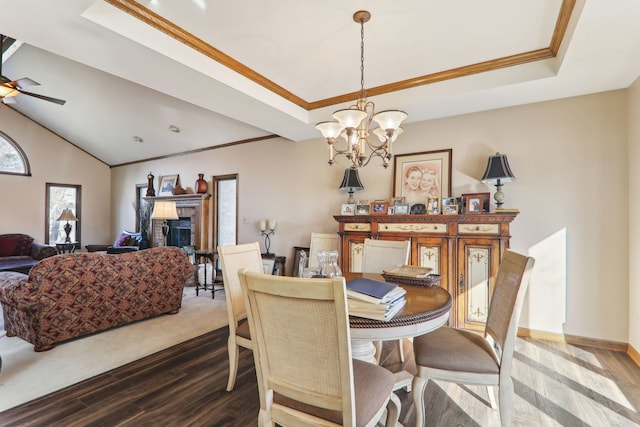 dining space with a raised ceiling, dark wood-type flooring, a fireplace, and crown molding