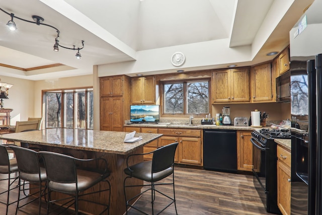 kitchen featuring a kitchen bar, black appliances, brown cabinets, and a raised ceiling