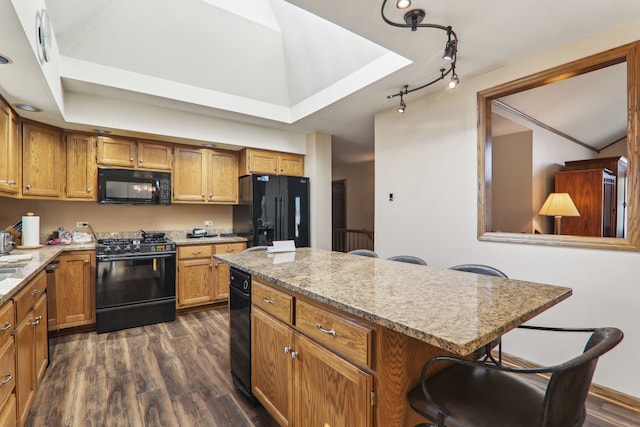 kitchen with brown cabinetry, dark wood finished floors, black appliances, a raised ceiling, and a center island