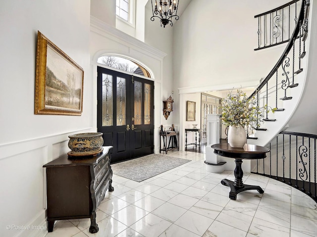 foyer entrance featuring marble finish floor, an inviting chandelier, a towering ceiling, and stairs