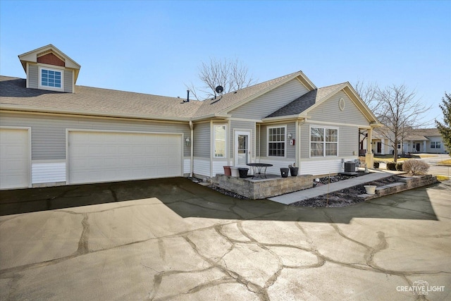 single story home with central AC, an attached garage, driveway, and roof with shingles