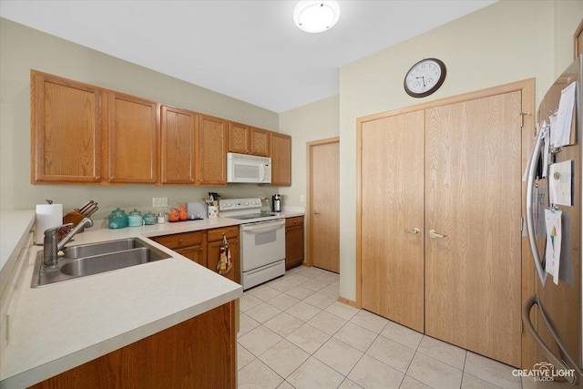 kitchen with white appliances, light tile patterned floors, a sink, light countertops, and brown cabinets