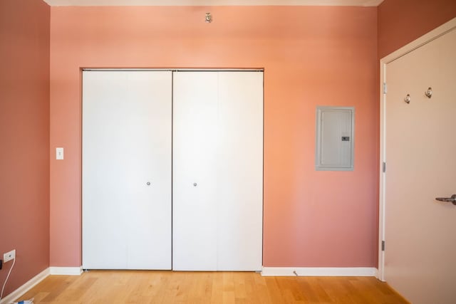 unfurnished bedroom with electric panel, a closet, light wood-type flooring, and baseboards