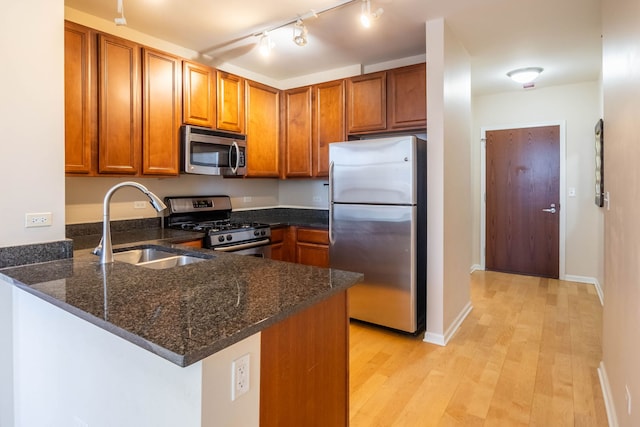 kitchen featuring dark stone countertops, brown cabinets, appliances with stainless steel finishes, a peninsula, and a sink