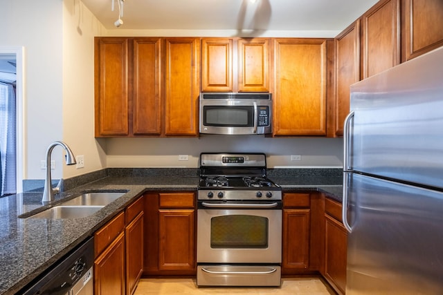 kitchen with brown cabinets, appliances with stainless steel finishes, dark stone counters, and a sink