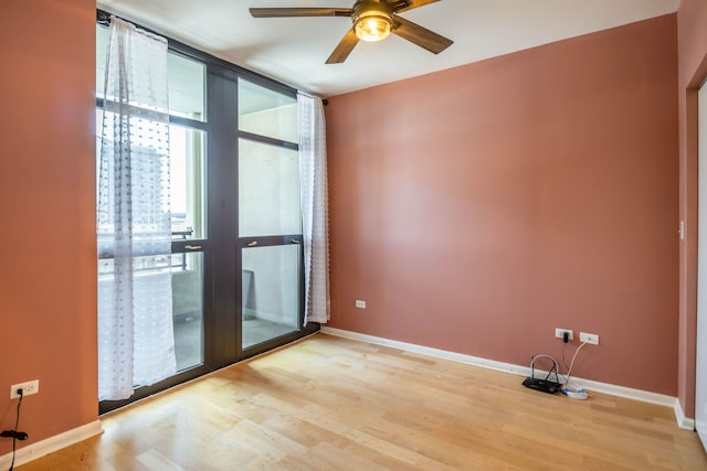 unfurnished room with expansive windows, baseboards, light wood-style flooring, and a ceiling fan