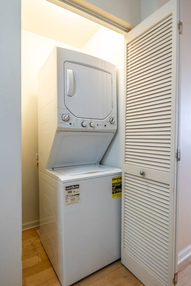 laundry area featuring laundry area, stacked washer and dryer, light wood-style floors, and baseboards