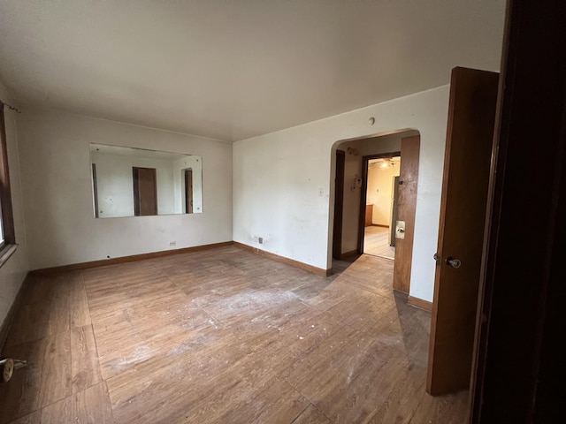 spare room featuring arched walkways, baseboards, and hardwood / wood-style floors