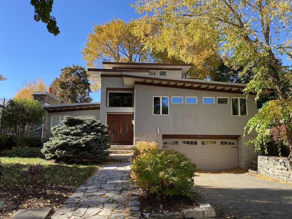 prairie-style house with a garage, driveway, stone siding, entry steps, and stucco siding