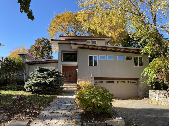 prairie-style house with a garage, driveway, stone siding, entry steps, and stucco siding