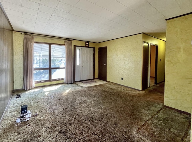 unfurnished living room featuring visible vents, crown molding, a textured wall, and carpet floors