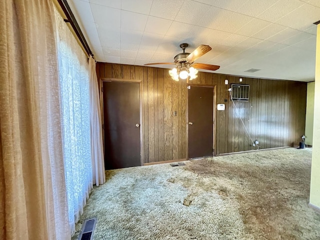 carpeted spare room with visible vents, wood walls, and a ceiling fan