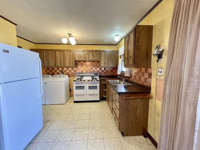 kitchen featuring white appliances, a sink, decorative backsplash, dark countertops, and independent washer and dryer