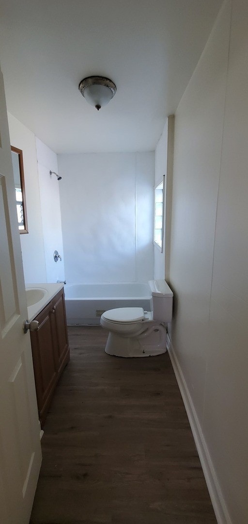 bathroom featuring baseboards, washtub / shower combination, toilet, wood finished floors, and vanity