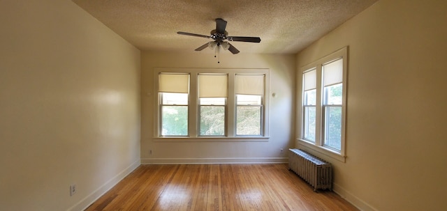 empty room with hardwood / wood-style flooring, a textured ceiling, radiator heating unit, baseboards, and ceiling fan