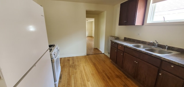 kitchen with a sink, dark countertops, white appliances, light wood-style floors, and baseboards