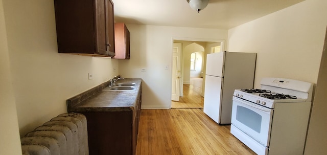 kitchen with light wood-style flooring, a sink, white appliances, radiator, and baseboards