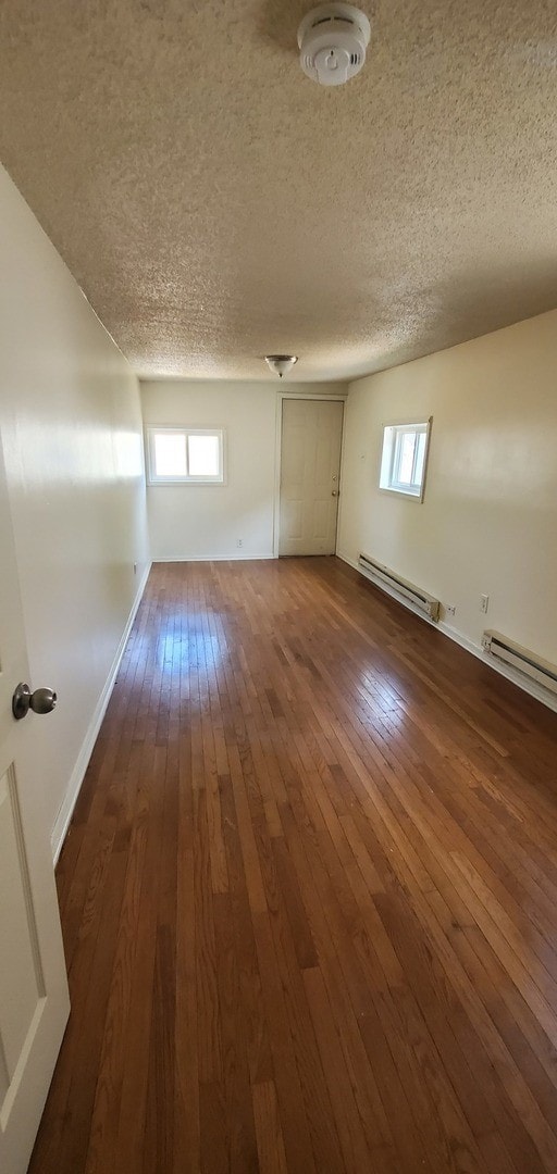 unfurnished room featuring a textured ceiling, dark wood-type flooring, a wealth of natural light, and a baseboard radiator