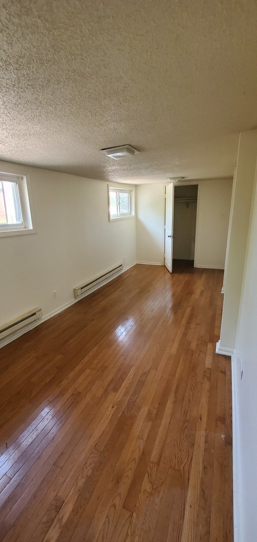 basement featuring plenty of natural light, wood-type flooring, and a baseboard radiator