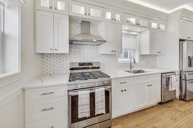 kitchen with white cabinets, appliances with stainless steel finishes, wall chimney range hood, and a sink