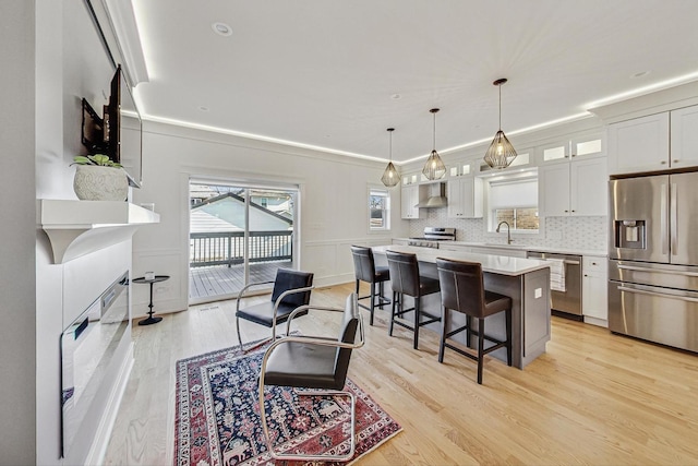 kitchen with light countertops, appliances with stainless steel finishes, a kitchen bar, wall chimney exhaust hood, and a center island