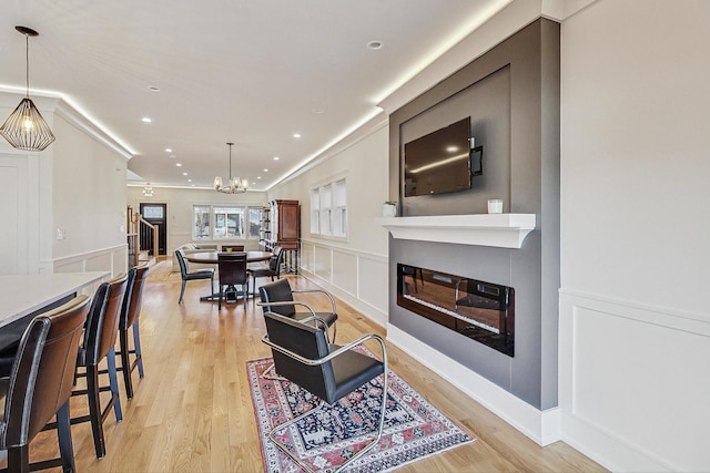 living room with light wood-type flooring, a notable chandelier, recessed lighting, a large fireplace, and a decorative wall