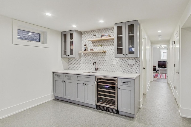 bar featuring beverage cooler, decorative backsplash, baseboards, and a sink