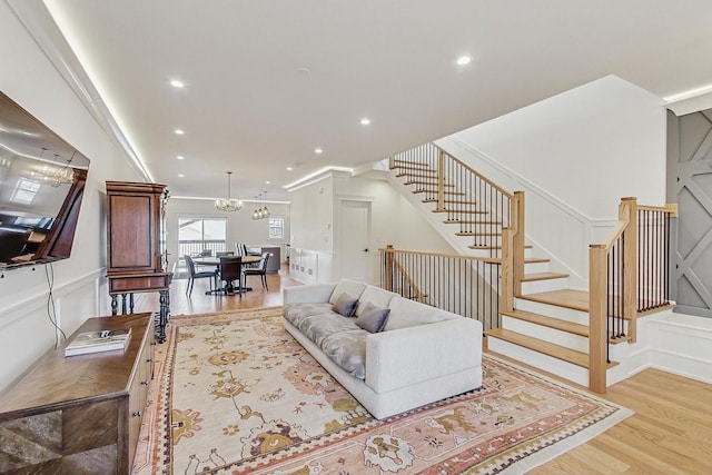 living room with light wood-type flooring, a notable chandelier, recessed lighting, stairway, and a decorative wall