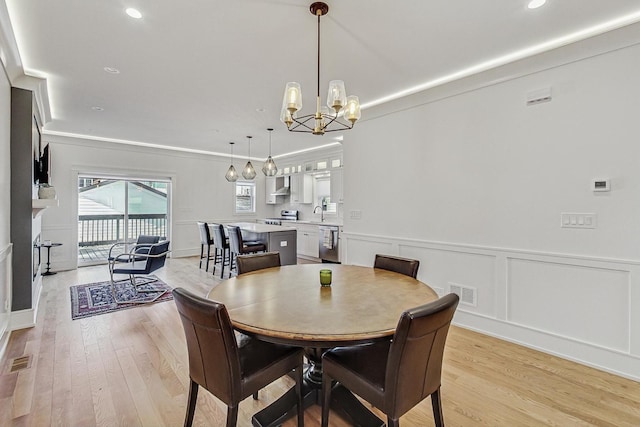 dining room with an inviting chandelier, light wood-style flooring, a decorative wall, and visible vents