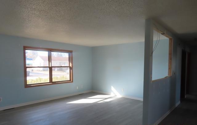 unfurnished room with dark wood-style floors, a textured ceiling, and baseboards