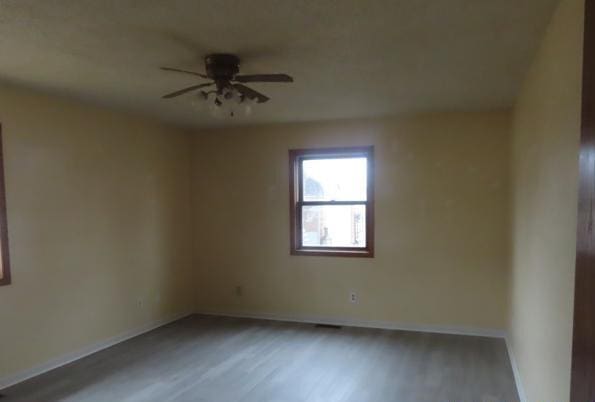 empty room with baseboards, wood finished floors, and a ceiling fan