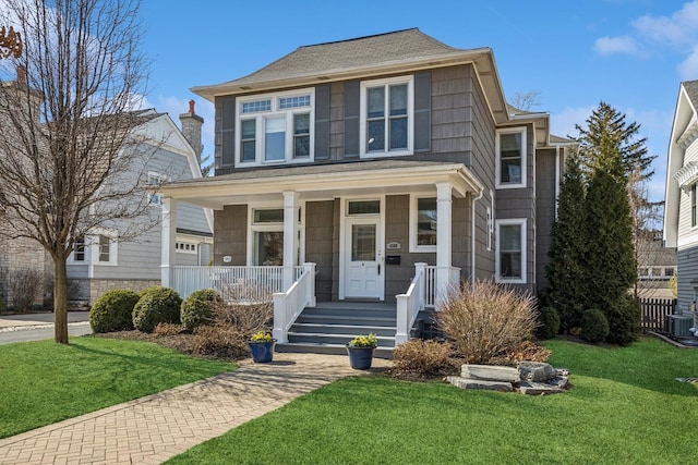 view of front of house with covered porch, central AC, a front yard, and a shingled roof