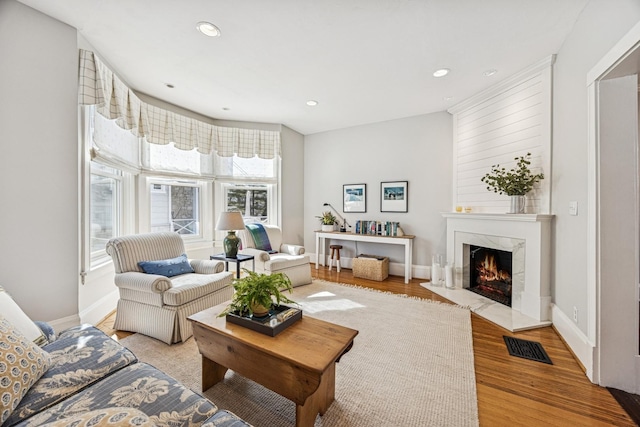 living area featuring baseboards, visible vents, light wood-style flooring, recessed lighting, and a high end fireplace