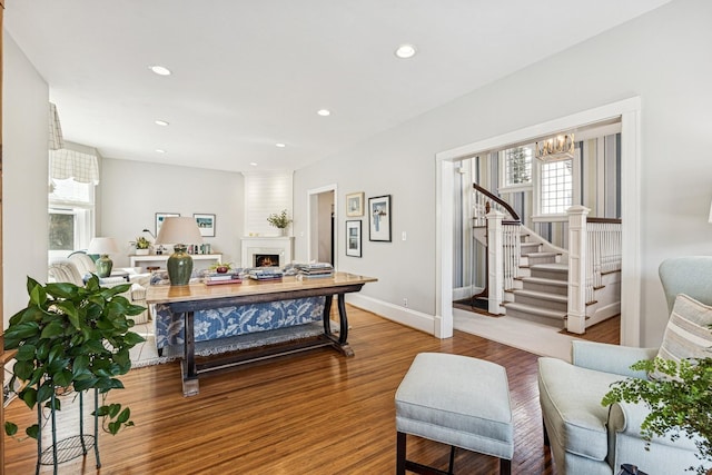 interior space featuring a lit fireplace, stairs, an inviting chandelier, and wood finished floors